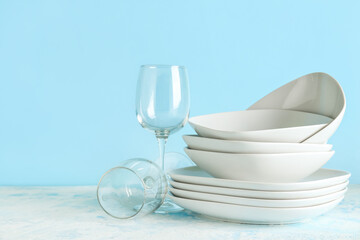 Clean glasses, bowls and plates on blue grunge table against color wall