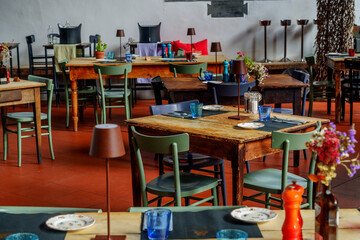Close-up of rustic dining room tables, vintage dishes, and colorful mismatched chairs