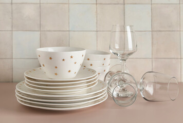 Clean glasses with plates, bowls and napkin on beige table against tile wall