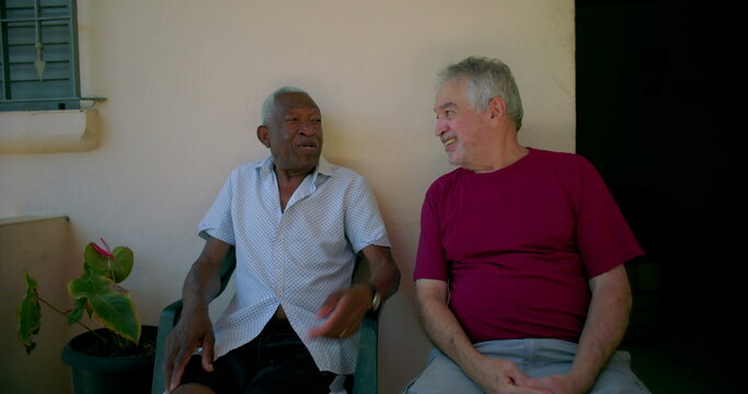 Elderly African American man smiling and chatting with a friend on outdoor patio, enjoying a friendly and relaxed social moment