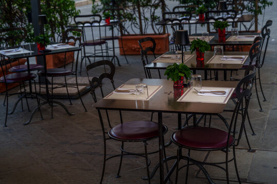 Outdoor café tables, black metal chairs, set for guests, potted herbs, relaxed patio atmosphere