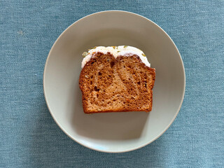 Slice of iced cake served on plate over fabric surface. Concept of homemade simplicity, calm indulgence, and visual balance in minimal food photography composition.
