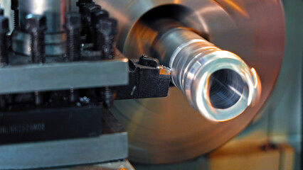 Lathe machine cutting rotating metal part. Close-up of a lathe machine in action, precisely cutting a rotating cylindrical metal workpiece in an industrial workshop.