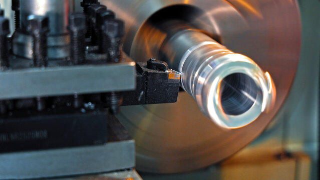 Lathe machine cutting rotating metal part. Close-up of a lathe machine in action, precisely cutting a rotating cylindrical metal workpiece in an industrial workshop.