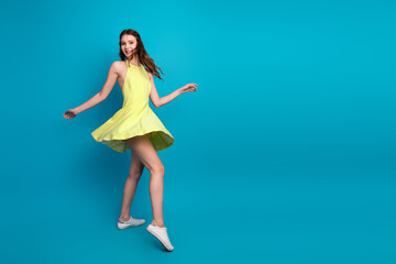 Young brunette woman spinning playfully in a vibrant yellow dress against a bright blue background