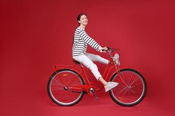 Smiling woman riding bicycle on red background. Space for text © New Africa