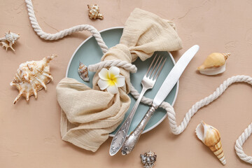 Beautiful table setting with plate, cutlery and marine decor on beige background