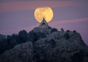 Full Moon Rising Behind a Mountain Chapel at Twilight