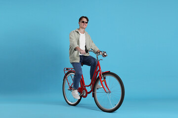 Fototapeta premium Handsome man riding red bicycle on light blue background