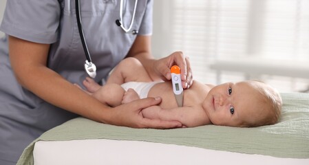 Pediatrician examining little child with thermometer in hospital, closeup. Checking baby's health
