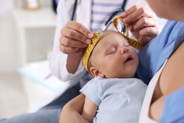 Mother and her cute little child having appointment with pediatrician in hospital, closeup. Doctor measuring baby's head