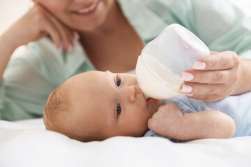 Mother feeding her newborn baby with bottle on bed at home, closeup