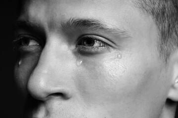 Obraz premium Sad man crying on dark background, closeup. Black and white effect