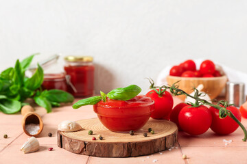 Bowl of tasty ketchup, fresh vegetables and basil leaves on beige tile table against white wall