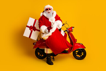 Santa Claus dressed in a festive costume joyfully sitting on a red scooter carrying gifts against a vibrant yellow background.