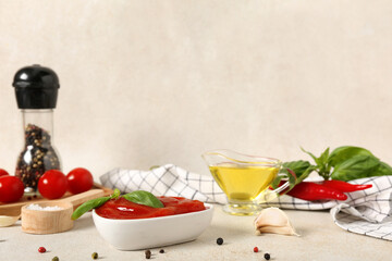 Bowl of tasty ketchup with garlic, fresh vegetables, peppercorns and basil leaves on light background