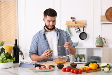 Cooking process. Young man seasoning dish at table in kitchen