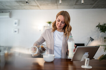 Woman eating breakfast cereal using digital tablet