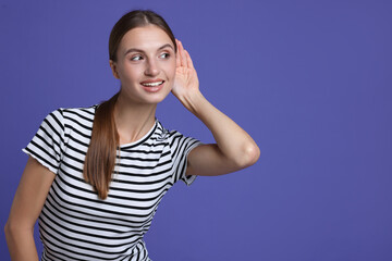 Fototapeta premium Woman showing hand to ear gesture on purple background, space for text