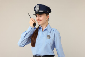 Young policewoman in uniform with walkie talkie on light grey background
