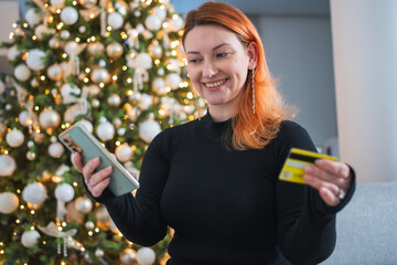 Christmas shopping. Woman shopping online holding smartphone paying with gold credit card for Christmas presents gifts. Girl buying on Internet enter credit card details. Christmas winter holidays