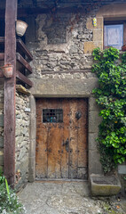 Vintage wooden door with metal grid set in an old stone wall of a rustic house. Ivy climbing on the wall and aged textures create a historical countryside atmosphere