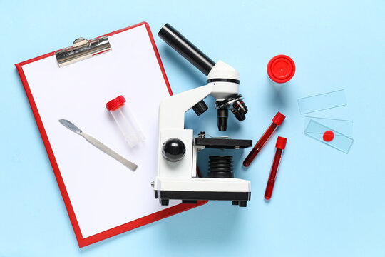 Modern microscope with clipboard, test tubes, blood samples, scalpel and slides on blue background