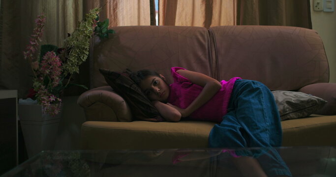 Young girl lying on a couch indoors, embodying solitude and emotional distance, reflecting themes of childhood loneliness, depression, mental health struggles, and introspection