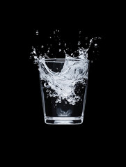 Water splashes dramatically from a glass against a black background