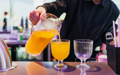 A bartender pouring a vibrant margarita into a chilled coupe glass, orange peel twist and salt rim visible, moody bar lighting with elegant presentation and negative space.
