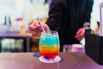A bartender pouring a vibrant margarita into a chilled coupe glass, orange peel twist and salt rim visible, moody bar lighting with elegant presentation and negative space.