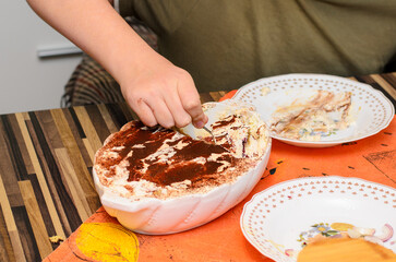 Person's hand scooping dessert from a serving dish with a small spoon