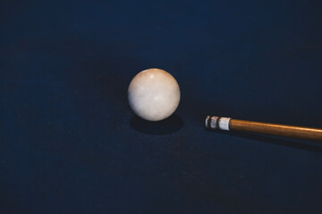 Close-up of cue stick striking the white ball in billiards. Hitting the cue ball on a blue pool table. Focused moment before cue ball impact. Precision cue shot in an american pool game.