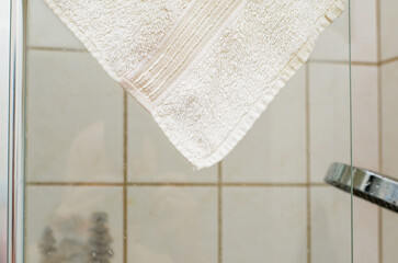 Corner of white terry cloth towel hanging on wet glass shower door