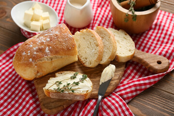 Sliced bread with butter, thyme and jug of cream on wooden background