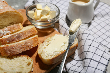 Wooden board with sliced bread, butter and jug of cream on grey grunge background