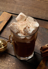 A glass of hot chocolate or cocoa with lots of cinnamon-dusted marshmallows on a dark background. A cozy winter drink.