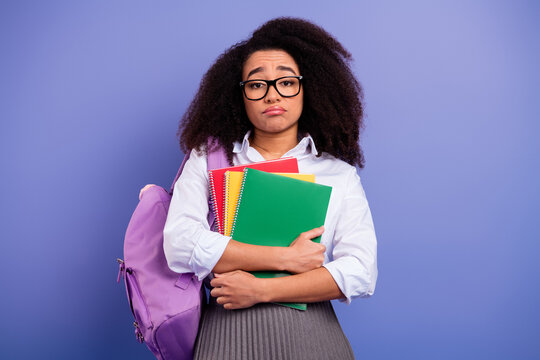 Young student with colorful notebooks and a backpack expressing a thoughtful mood on a purple background - Powered by Adobe
