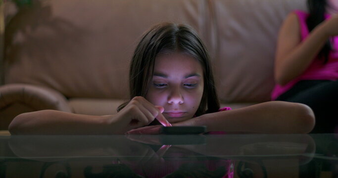 Child engrossed in smartphone, lying on table in living room, showing signs of social media addiction, disconnected from surroundings, highlighting digital dependency