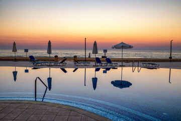 Swimming pool with sun loungers and umbrellas at sunset by the sea