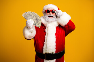 Santa Claus wearing sunglasses holding cash and smiling on a bright yellow background festive holiday portrait