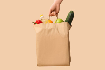 Woman holding paper bag with vegetables, fruits and bottle of oil on beige background