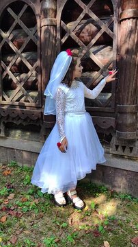 A girl in a white dress and a veil, the image of a scary bride, moves like a zombie on the street, in the park on Halloween