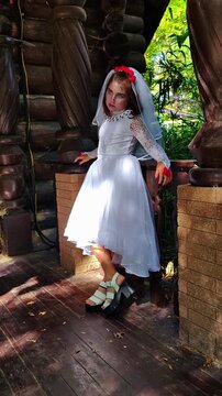 A girl in a white dress and a veil, the image of a scary bride, moves like a zombie on the street, in the park on Halloween