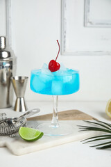 Glass of Blue Lagoon cocktail with bartender supplies on white background