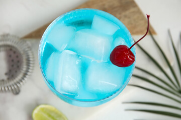 Glass of Blue Lagoon cocktail with cherry on white background