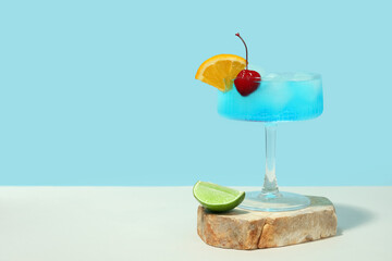 Glass of Blue Lagoon cocktail with citrus fruit slices on white table against blue wall