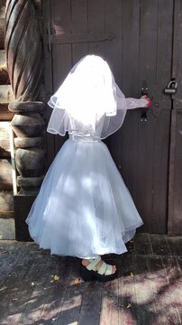 A girl in a white dress and a veil, the image of a scary bride, moves like a zombie on the street, in the park on Halloween