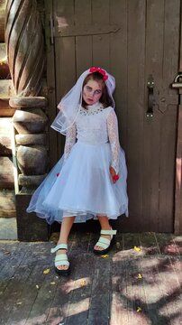 A girl in a white dress and a veil, the image of a scary bride, moves like a zombie on the street, in the park on Halloween