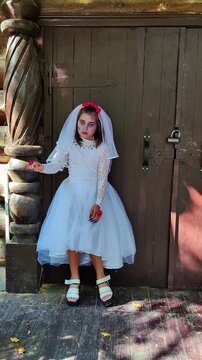 A girl in a white dress and a veil, the image of a scary bride, moves like a zombie on the street, in the park on Halloween